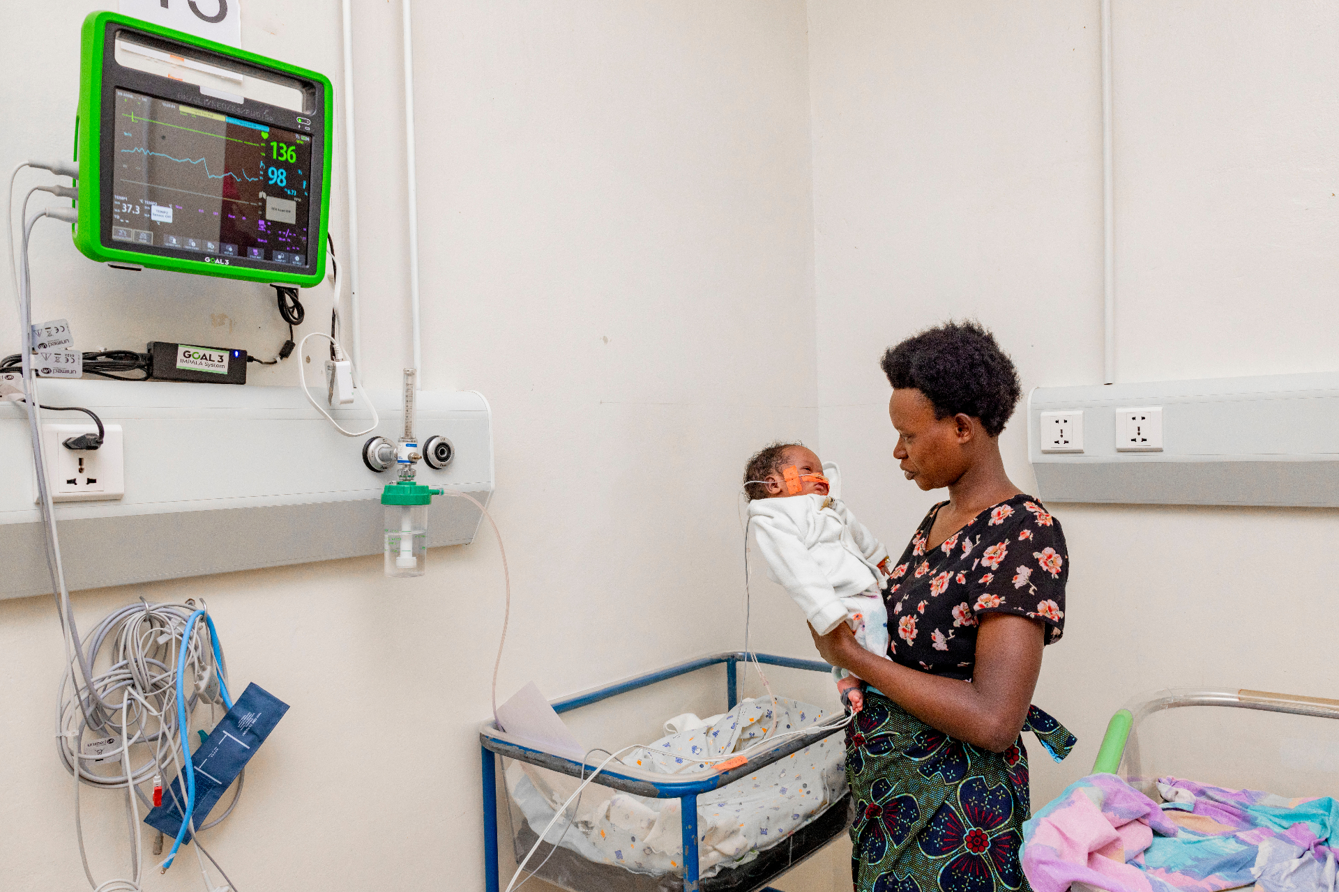 Mother holding her baby beside a GOAL 3 IMPALA patient monitor at Nyamata hospital